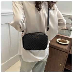 Detail of black quilted crossbody bag with golden metal bar and elegant V-shaped stitching