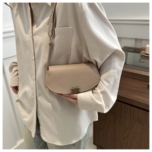 Close-up of minimalist beige saddle bag with gold metal buckle on a shoulder strap