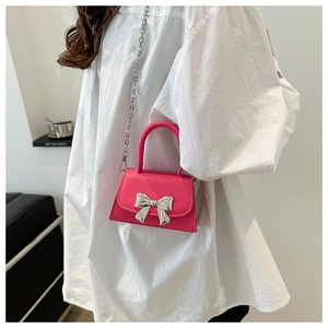 Detail of rose pink mini bag with large silver bow, chain strap, and top handle