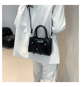 Détail du sac à main noir brillant avec perles et logo sur un costume blanc chic