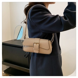 Close-up of beige leather baguette bag featuring a large gold metal buckle on shoulder