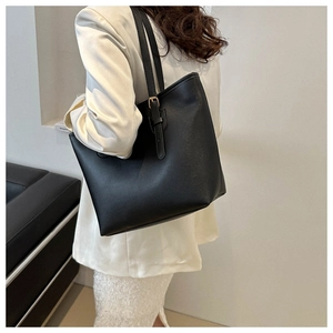 Detail of minimalist black leather tote bag with elegant gold buckle on white blazer