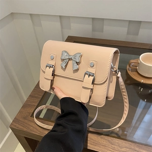 Fashionable beige faux leather shoulder bag with silver bow accent and buckle straps