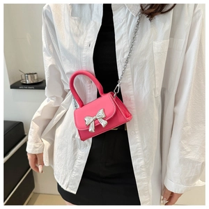 Detail of mini pink crossbody bag featuring a silver bow accent and metallic chain strap