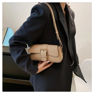 Detail view of a beige crossbody bag with a wide strap and gold buckle on a model