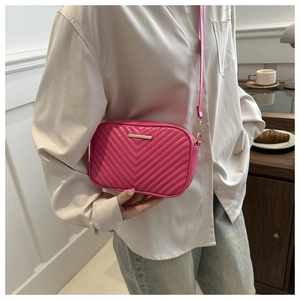 Close-up of fuchsia chevron quilted crossbody bag with gold hardware worn by model