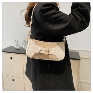 Close-up of a beige baguette bag with a gold square metal buckle on a model shoulder