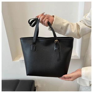 Detailed close-up of matte black leather tote bag featuring golden metal buckles and logo