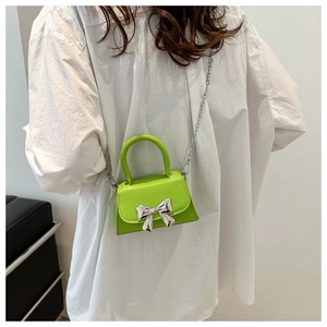 Detailed view of neon green mini crossbody bag with silver bow on a female model