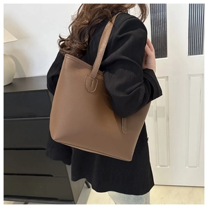 Detail view of a brown leather tote bag with thin straps and a minimalist embossed logo