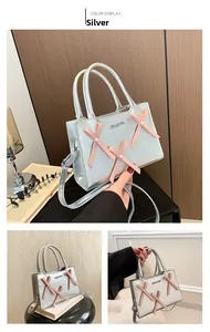 Détail du sac argenté avec nœuds en ruban rose, perles blanches et logo métallique gravé