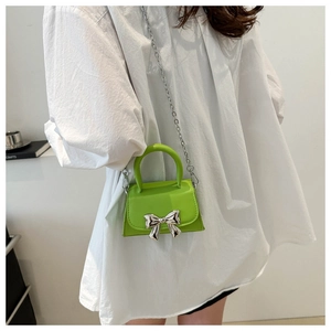 Detail of neon green mini bag with silver metal bow accent and chain shoulder strap