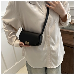 Chique zwarte lederen zadeltas met gouden magnetische gesp gedragen als crossbody tas