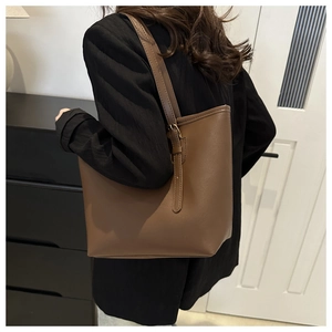 Side view of a brown faux leather tote bag worn by a model in a black suit