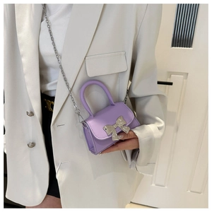 Detail of purple crossbody bag with silver bow accent on a white blazer background