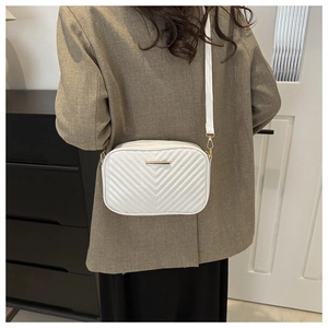 White quilted crossbody bag with golden hardware shown on a model in a minimalist room