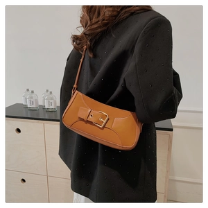Brown leather baguette underarm bag with gold buckle detail worn by a model in a room