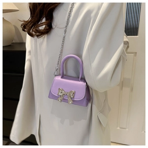 Detail of light purple mini crossbody bag with silver metal bow and chain strap on model