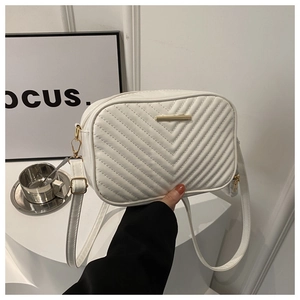 Detailed view of the white quilted crossbody bag with golden metal trim and V-shaped stitching