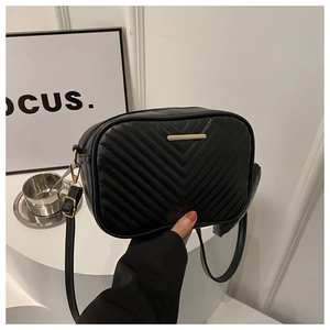 Detail of black quilted PU leather crossbody bag with V-shaped stitching and gold hardware