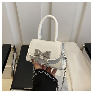 Close-up of white mini handbag featuring a metallic silver bow and elegant chain strap