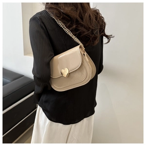 Detail der cremefarbenen Lackledertasche mit goldenem Herzschloss an einem Model