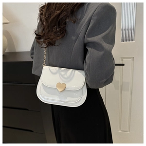 Detailansicht der glänzenden weißen Lackledertasche mit goldenem Herzverschluss und Kette