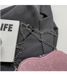 Close-up of pink sequined heart-shaped handbag with a silver chain on grey fabric