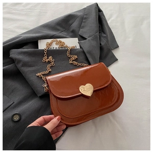 Detailaufnahme der braunen Lackleder-Satteltasche mit goldenem herzförmigem Metallverschluss