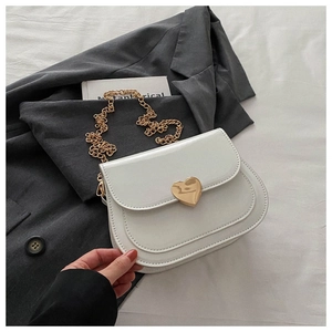 Detailansicht der weißen Lackleder-Satteltasche mit goldenem Herzschloss und Kettenriemen