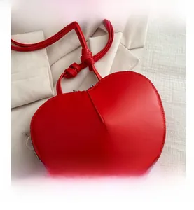 Detail of red heart-shaped shoulder bag featuring smooth leather texture and knotted strap