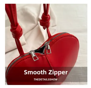 Detail of red heart-shaped bag showing smooth double metal zippers and PU leather texture