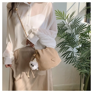 Dettaglio di una borsa a secchiello beige con catena dorata e ciondolo di peluche