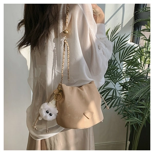 Dettaglio borsa a secchiello beige con catena dorata e ciondolo in peluche morbido