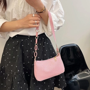 Pink woven crescent shoulder bag with chain detail on a model in a minimalist setting