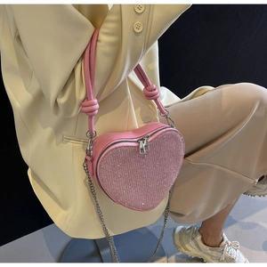 Detail view of pink heart-shaped sequin purse with metal chain and top handle on model