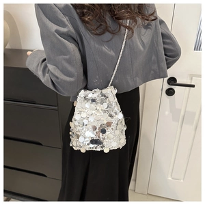 Detail view of silver sequin bucket bag with metal chain strap worn by a model