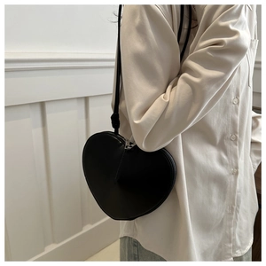 Close-up of a stylish black heart-shaped crossbody bag worn over a light shirt