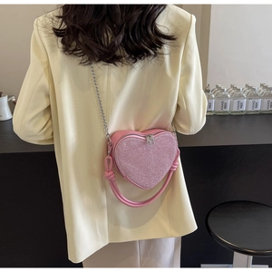 Detail view of heart-shaped sequin crossbody bag in pink with silver chain on model