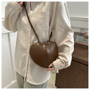 Detail of a brown leather heart-shaped crossbody bag worn with a casual cream shirt