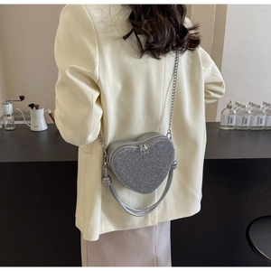 Detail of silver sequin heart bag with metallic chain strap worn over a beige blazer