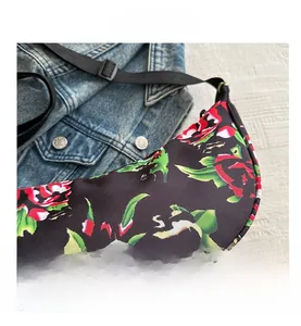 Detail view of crescent floral bag with red rose pattern and adjustable strap on denim background