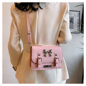 Detail of pink crossbody bag with silver bow buckle worn over a beige suit jacket