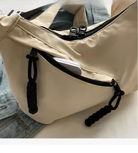 Detail of cream crossbody bag featuring black contrast zipper and tactical cord puller