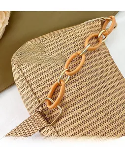 Close-up of amber resin chain strap on a woven straw crescent shoulder bag detail