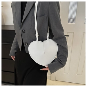 Minimalist white heart-shaped leather shoulder bag worn by model in professional grey suit