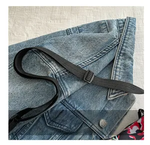 Detail of adjustable black woven shoulder strap on light blue washed denim dumpling bag