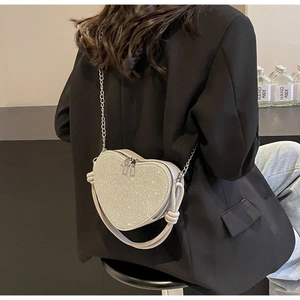 Detail of white heart-shaped sequin bag with chain strap and knotted handle worn by model