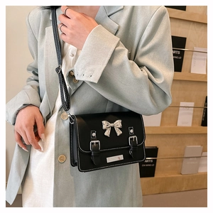 Detail of black leather crossbody bag with silver bow accent and retro buckle straps