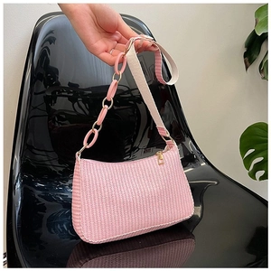 Pink woven crescent bag with gold chain and woven strap on a modern chair